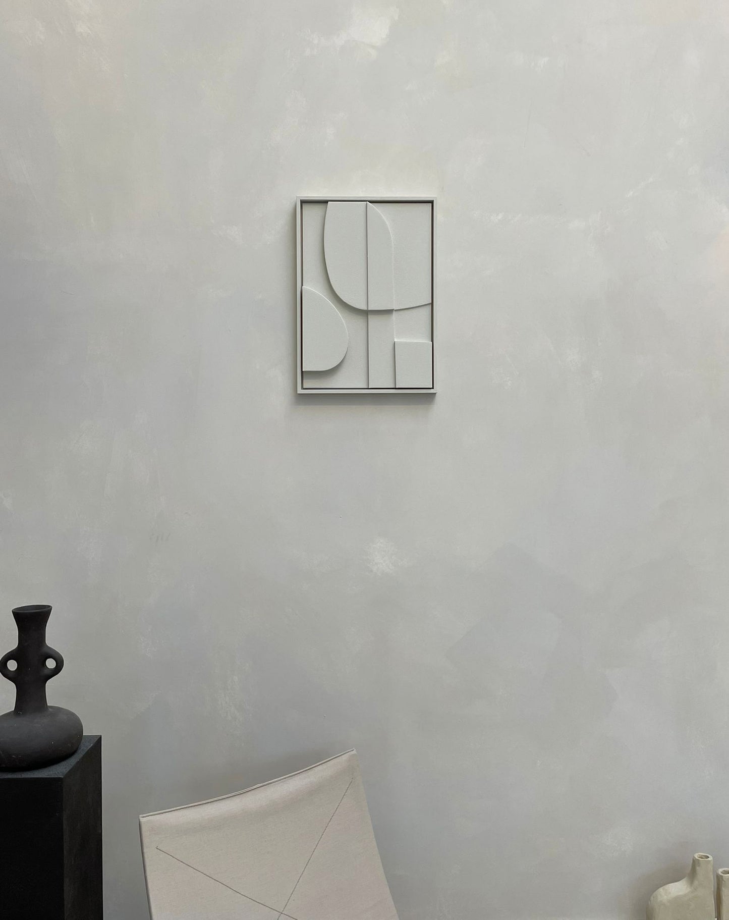 Minimalist wall art piece on a textured wall background, featuring abstract shapes in soft tones.